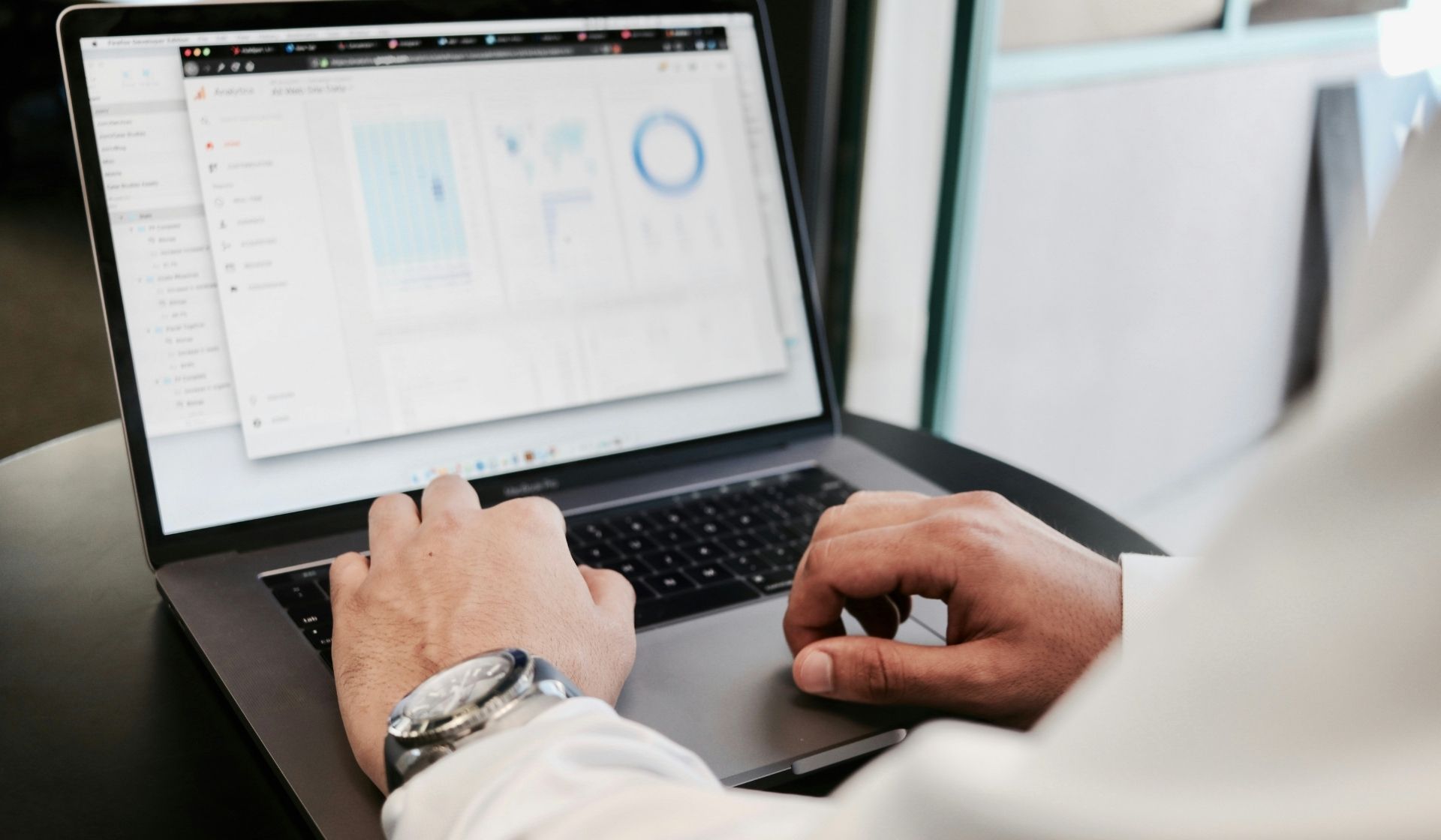 Personne utilisant un ordinateur portable affichant des tableaux de bord et graphiques de données dans un environnement professionnel.